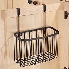 a black metal basket hanging on the side of a wooden wall next to two hooks