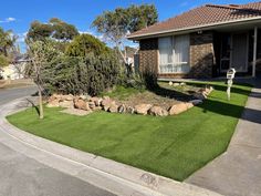 artificial grass in front of a house with rocks and trees on the side of the road