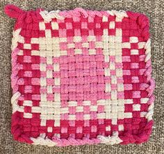 a pink and white crocheted square sitting on top of a carpeted floor