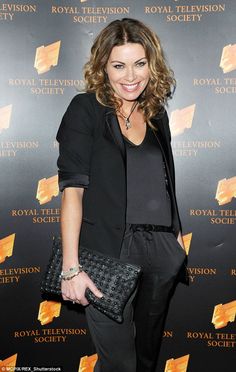 a woman standing in front of a red carpet holding a black purse and smiling at the camera