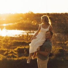 a man carrying a woman in his arms as the sun sets over a body of water