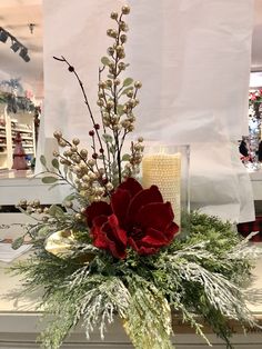 a vase filled with flowers and greenery on top of a white countertop next to a candle