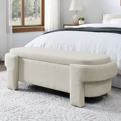 a white bed with a footstool sitting on top of it next to a window