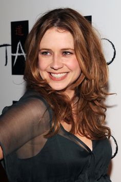 a woman with long brown hair smiling at the camera and wearing a sheer top on her shoulders