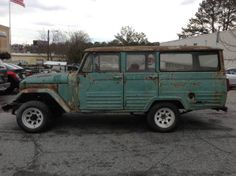 an old rusted green jeep is parked in a parking lot with other cars behind it