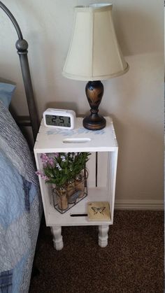 a night stand with a clock on it next to a lamp and flowers in a vase