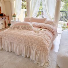 there is a bed with pink comforter and pillows on the floor next to a window