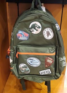 a green backpack with various stickers on it sitting on a shelf in a store