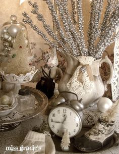 an assortment of silver and white items on a table with a clock in the middle