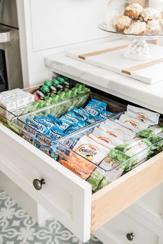 an open drawer in a kitchen filled with snacks and drinks on top of a counter