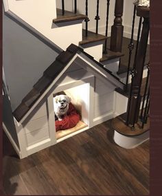 a dog is sitting in his house under the stairs at the bottom of the stairs