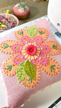 a pink and green decorative pillow sitting on top of a white table next to a sewing machine