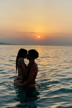 two people sitting in the water kissing each other at sunset on a body of water