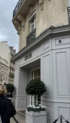 a woman is taking a photo of the exterior of a building with flowers in pots