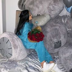 a woman sitting on top of a bed holding a bouquet of roses next to a giant teddy bear