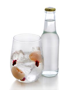 an empty glass with ice and fruit in it next to a bottle filled with water