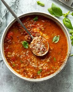 a bowl of tomato soup with basil leaves on the side and a spoon in it