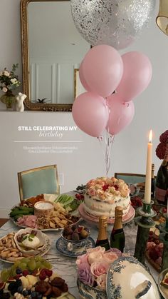 a table topped with pink balloons and plates filled with food next to a mirror on the wall