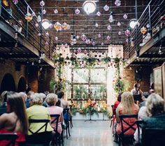 people are sitting in chairs at the end of a room with lights hanging from the ceiling