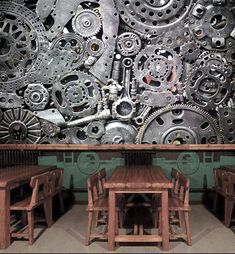 a large metal wall with lots of gears on it and wooden tables in the middle