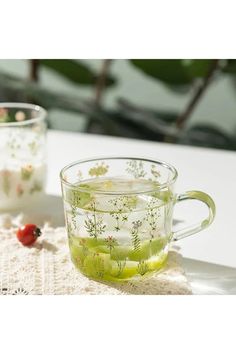 two glass mugs filled with green tea on top of a table