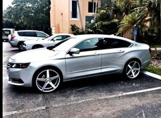 a silver car parked in a parking lot next to a building with palm trees behind it