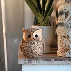 an owl figurine sitting on top of a table next to a potted plant