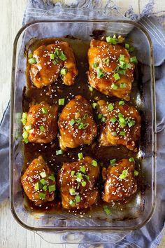 chicken wings with sesame seeds and green onions in a glass dish on a wooden table