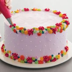 a person is decorating a cake with flowers on the frosting and sprinkles