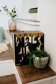 the rolling stones now album sitting on top of a wooden shelf next to a potted plant