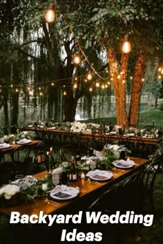 an outdoor dinner table set up with lights strung from the trees and greenery on the tables