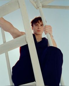 a young man sitting on top of a white wooden structure with his hands in the air