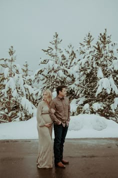 a man and woman standing next to each other in front of snow covered trees