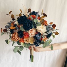 a woman holding a bouquet of flowers on top of a white sheet with leaves and foliage