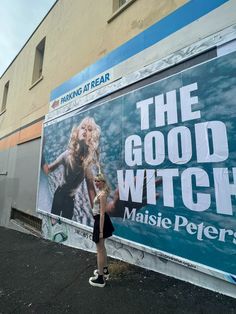 a woman standing in front of a movie poster on the side of a building that says the good witch