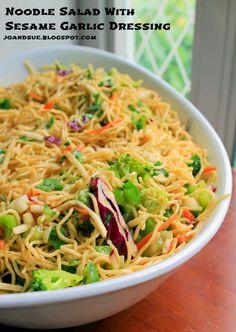 noodle salad with sesame garlic dressing in a white bowl on a wooden table next to a window