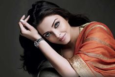 a woman in an orange and gold sari posing for the camera with her hands on her head