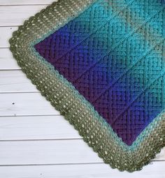 a blue and green knitted blanket sitting on top of a white wooden floor next to a wall