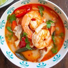 a bowl of soup with shrimp, peppers and cilantro on the side next to a lime wedge