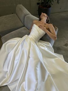 a woman in a white wedding dress laying on a couch with her head resting on the pillow