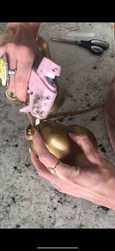 a person is working with some gold and pink ornaments on the counter top next to a pair of scissors