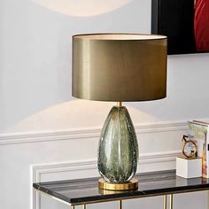 a table with a lamp on top of it next to a book shelf and pictures