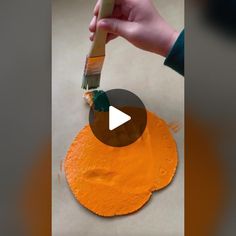 someone is painting an orange piece of paper with a paintbrush on top of it