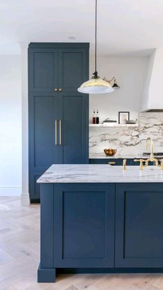 a kitchen with blue cabinets and marble counter tops, gold faucets and pendant lights