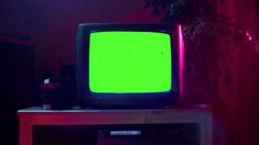 an old television with green screen sitting on top of a wooden table in front of a potted plant