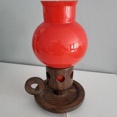 a red vase sitting on top of a wooden stand next to a white wall,