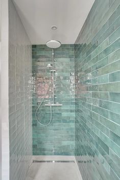 a walk in shower sitting next to a tiled wall and white floored bathroom with green tiles on the walls