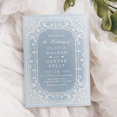 a blue and white wedding card sitting on top of a bed next to some flowers