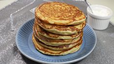 a stack of pancakes sitting on top of a blue plate next to a cup of yogurt