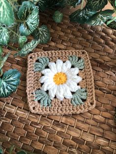 a crocheted square with a white flower on it next to a potted plant